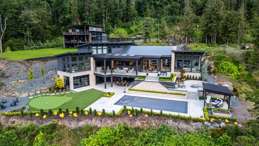Landscaping project of beautiful backyard with pool, artificial turf putting green, vibrant planting and fire pit.